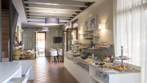 Ein Bereich für das Frühstücksbuffet mit verschiedenen Speisen, einer Sitzgelegenheit mit Stühlen und einem an der Wand befestigten Fernseher.