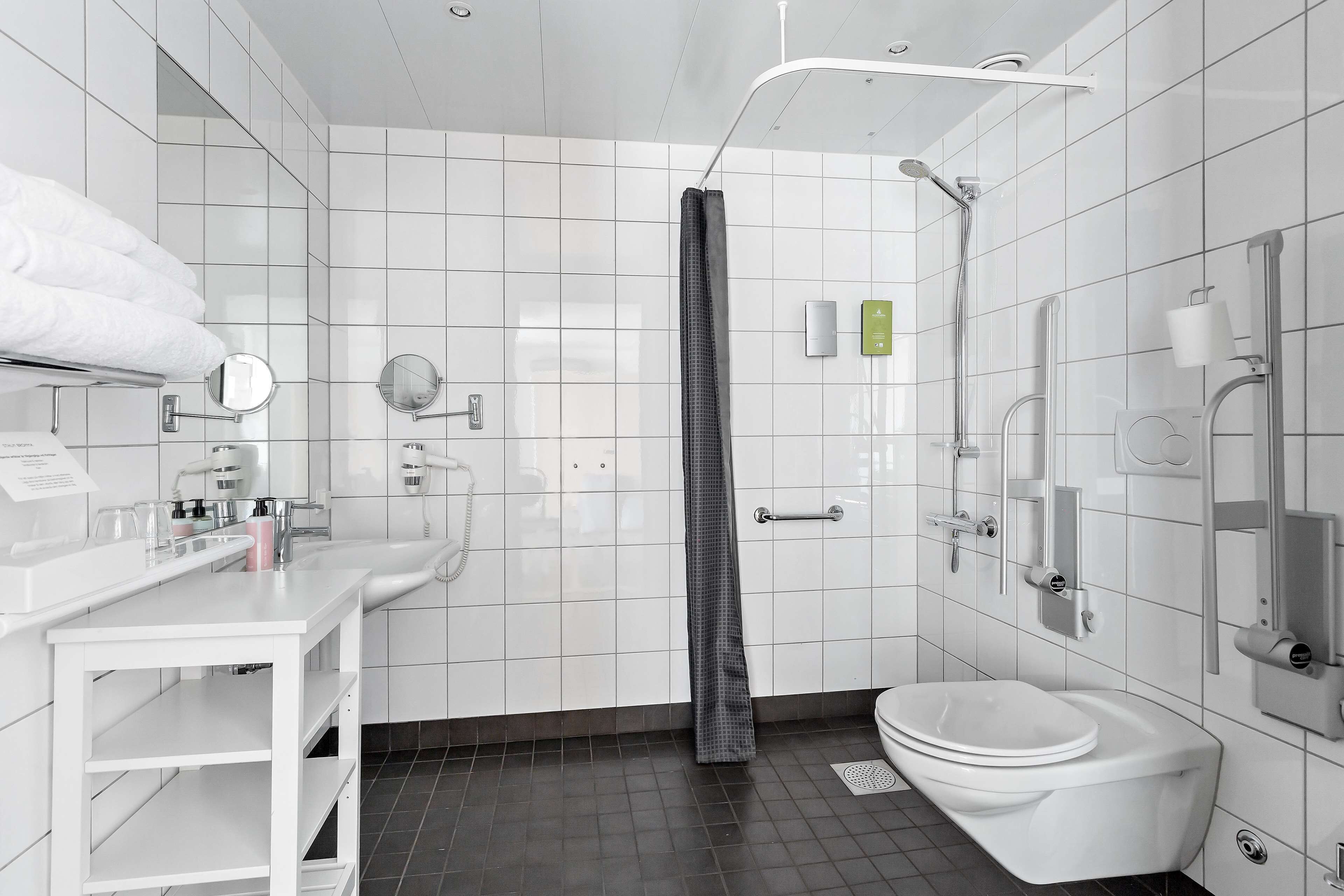 A modern bathroom with white tiles, a white sink, a toilet, and a shower area.