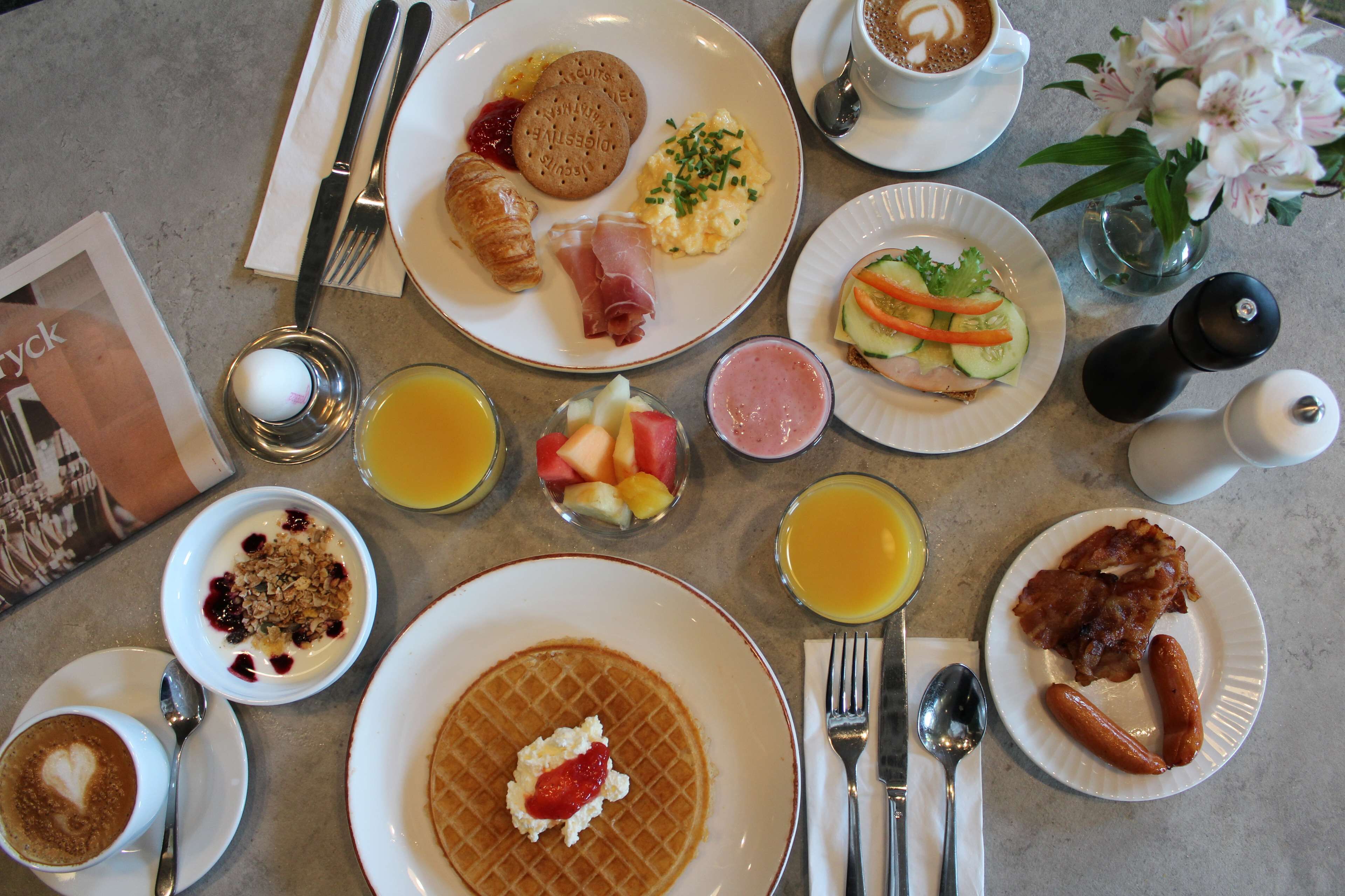 Una mesa de desayuno con diversos platos, como waffles, croissants y fruta.