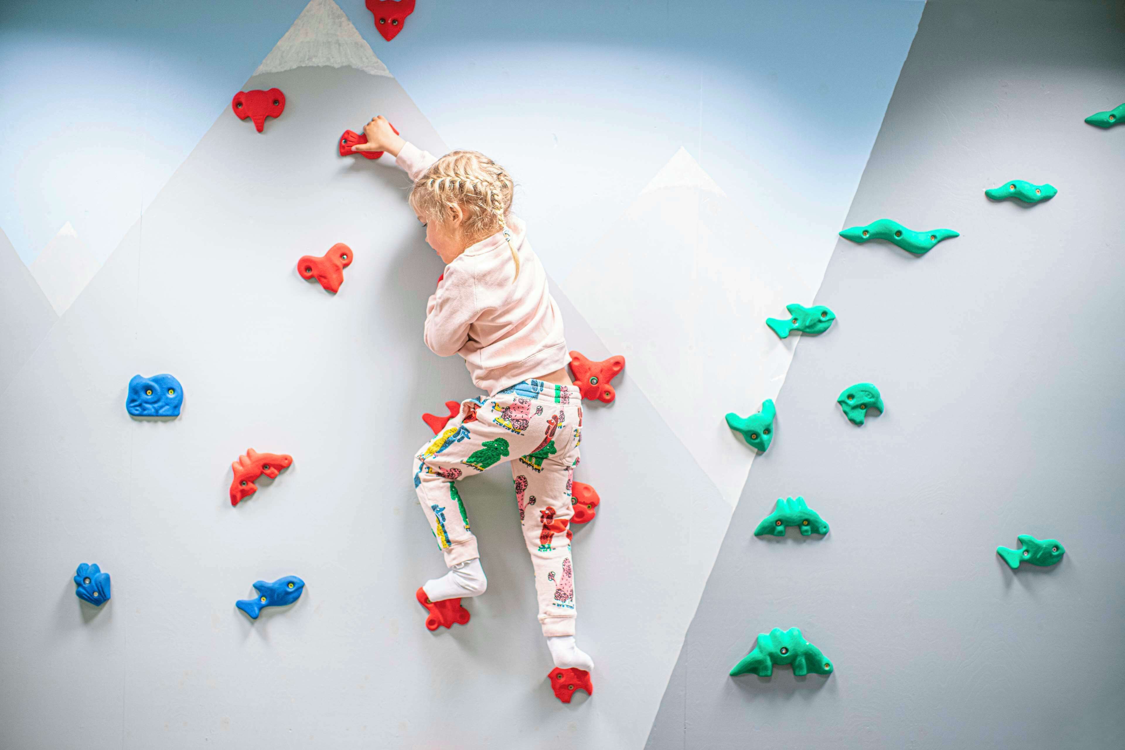 Un niño trepando por una pared con puntos de apoyo con forma de animales de colores.