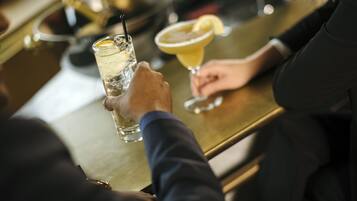 Un bar con una persona sosteniendo un vaso de una bebida transparente con hielo y una rodaja de limón, y otro vaso con una bebida amarilla adornada con una rodaja de limón.