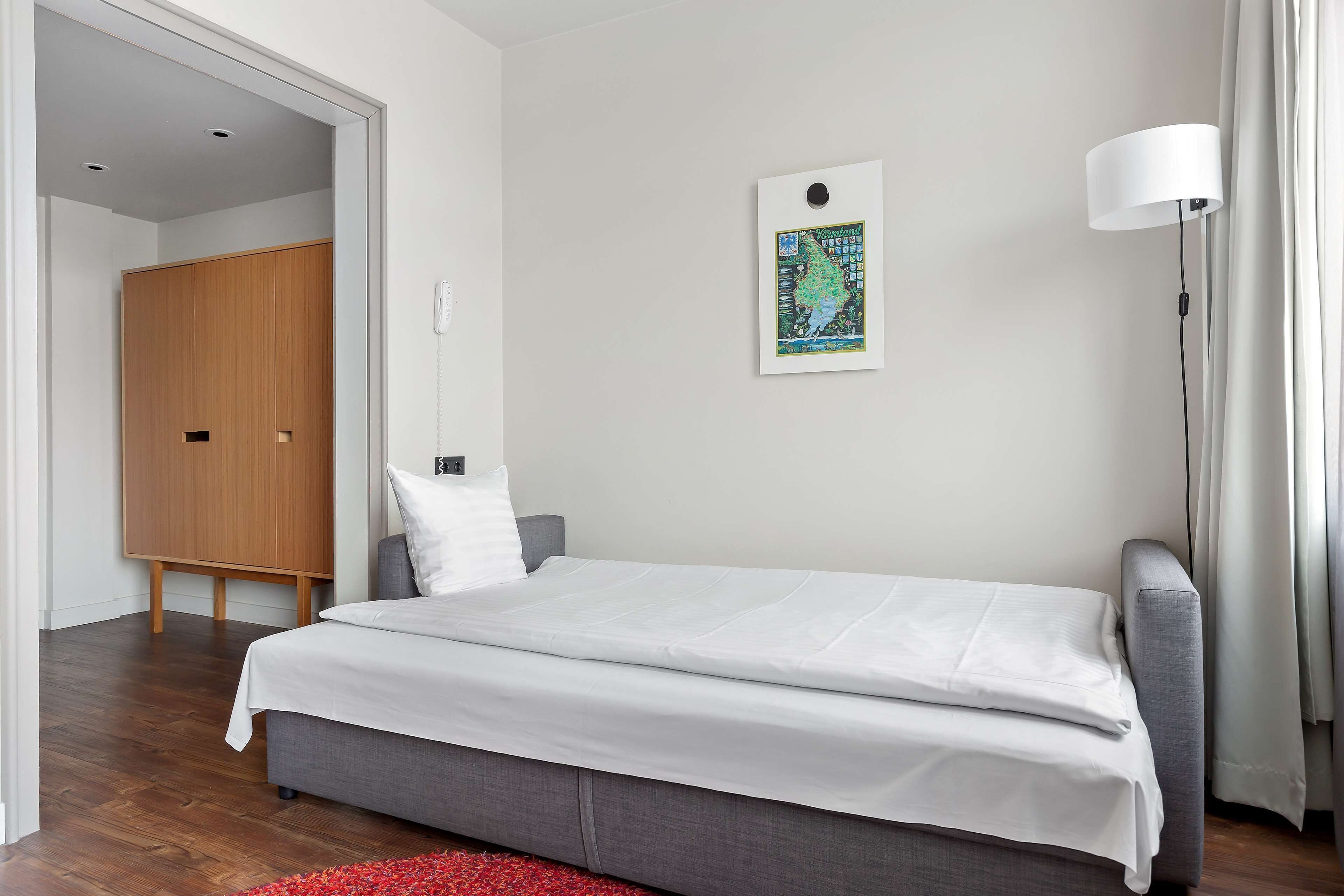 A modern bedroom with a grey sofa, a white bed, and a wooden wardrobe.