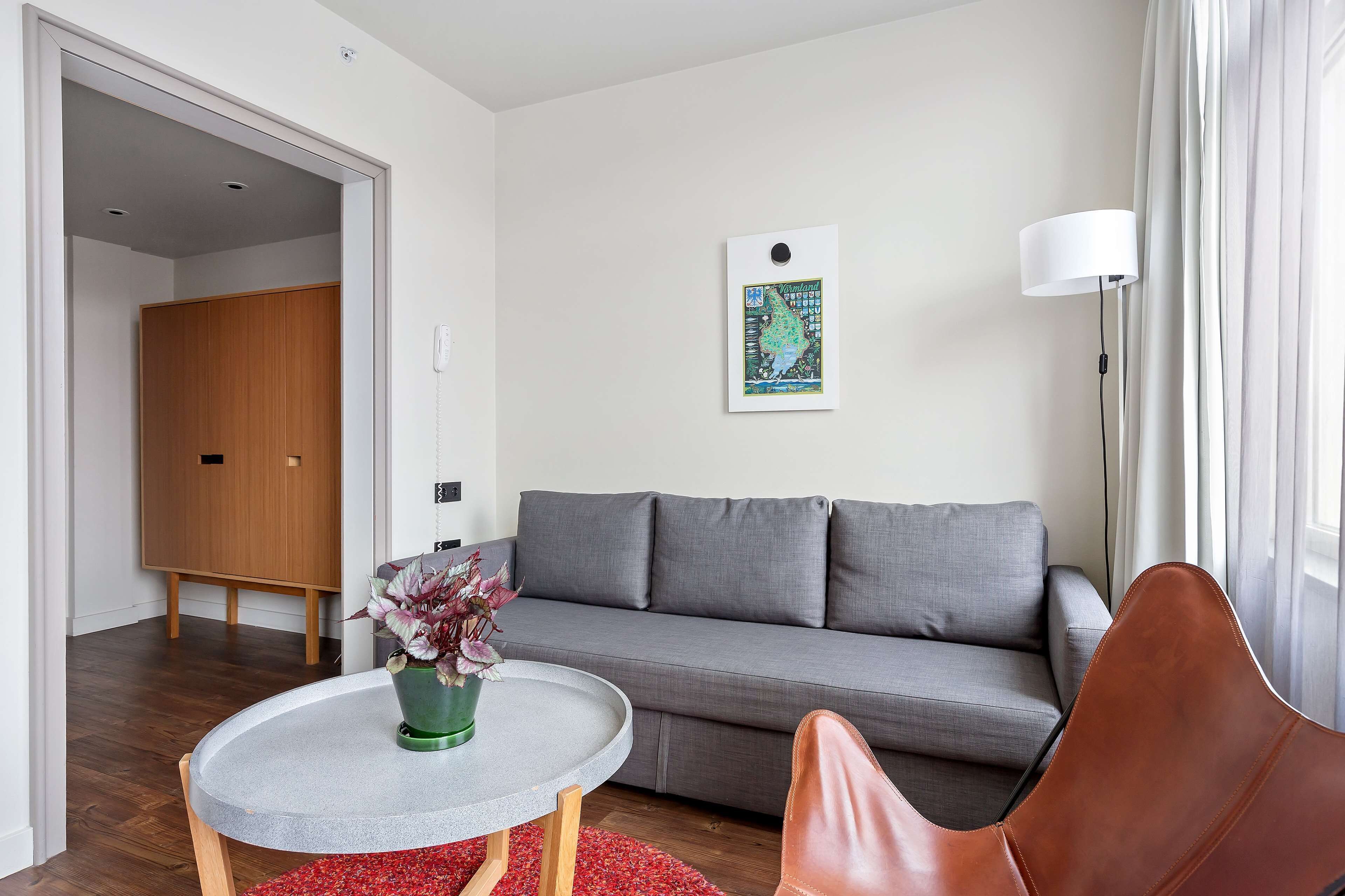 A modern living room with a grey sofa, a round table with a green plant, a brown leather chair, and a floor lamp.