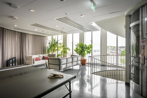 A modern hotel lobby with a ping pong table, seating area, potted plants, and a view of the city through large windows. - Best Western Plus Sthlm Bromma (Bromma)