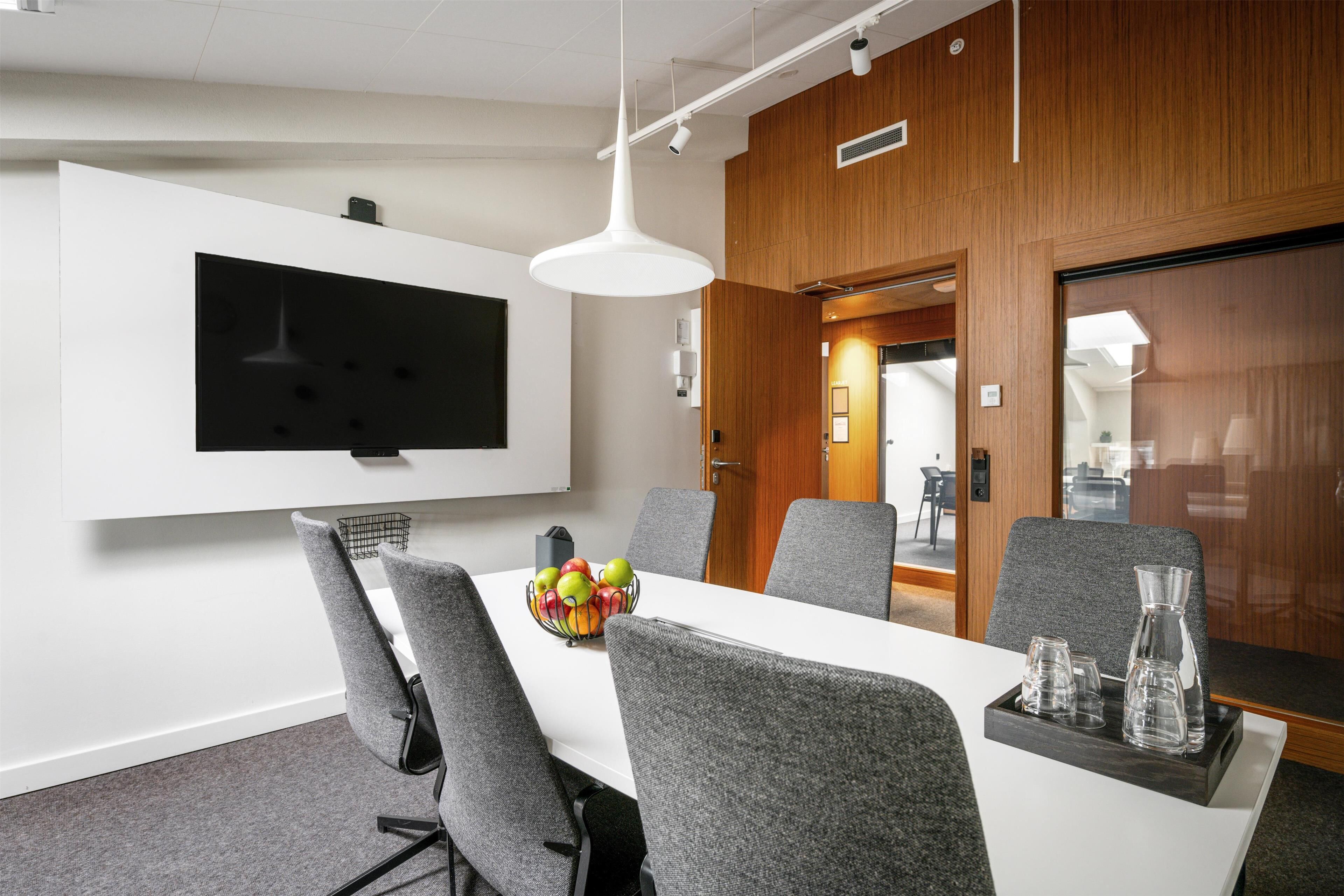 A conference room with a white table, grey chairs, a fruit bowl, and a white pendant light.