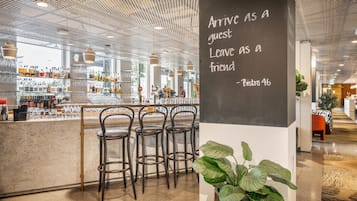 A modern bar area with a chalkboard sign, bar stools, and a variety of bottles and glasses on shelves.