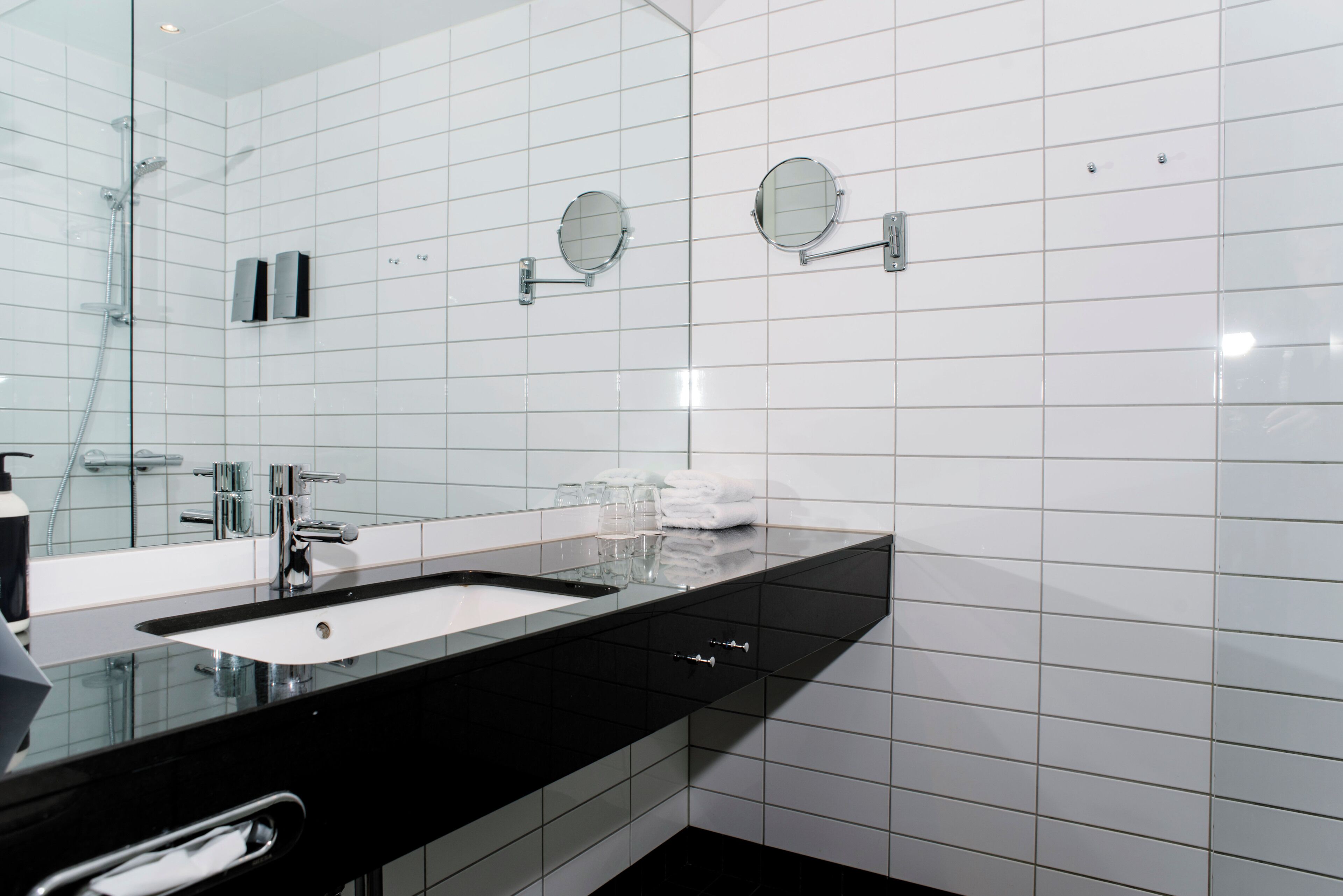 Un bagno moderno con un piano lavabo nero, due lavandini e un ampio specchio.