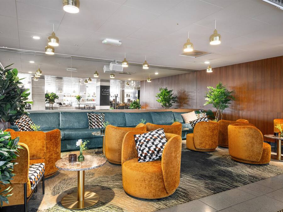 A modern lobby with a green sofa, orange armchairs, and a coffee bar in the background.