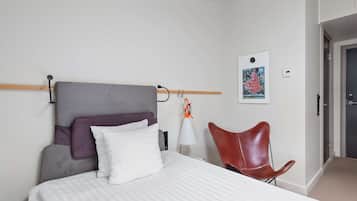 A hotel room with a bed, a chair, a lamp, and a wall-mounted artwork.