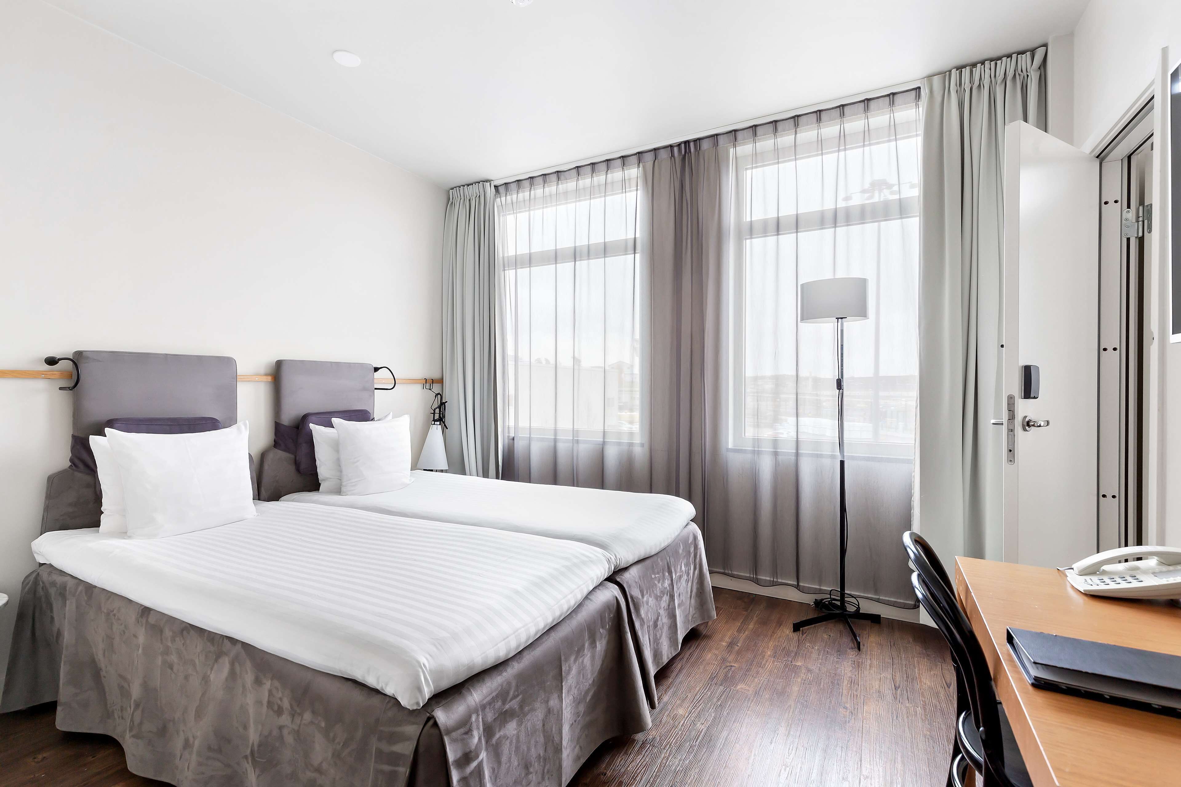 Quarto de hotel com duas camas, uma escrivaninha com telefone e uma luminária.