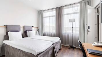 Quarto de hotel com duas camas, uma escrivaninha com telefone e uma luminária.