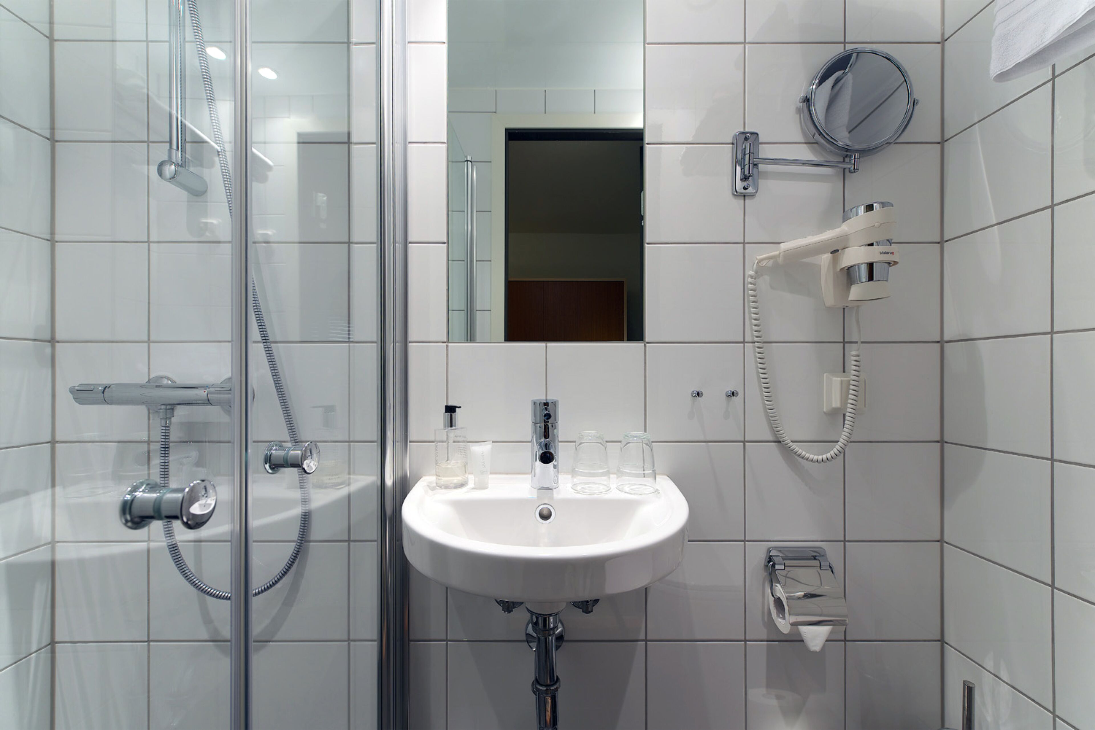 A modern bathroom with a glass-enclosed shower, a white sink, and a mirror.