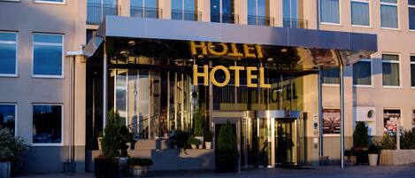 A hotel entrance with a glass facade, a prominent 'HOTEL' sign, and potted plants at the entrance.