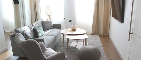 A modern living room with a grey sofa, a round coffee table, and a grey armchair.