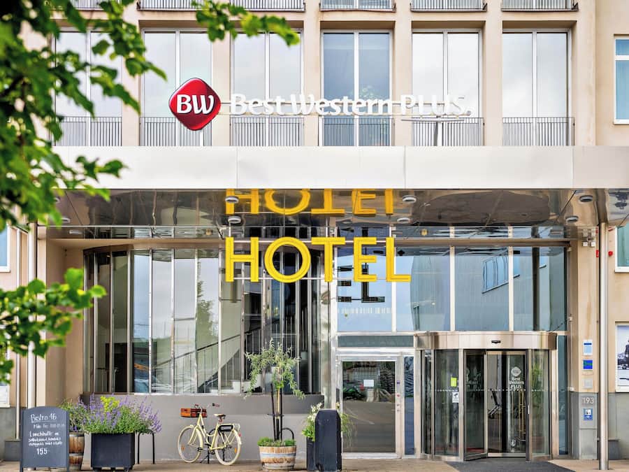 L'ingresso di un hotel con facciata in vetro, un cartello di Best Western Plus e una bicicletta parcheggiata all'esterno.