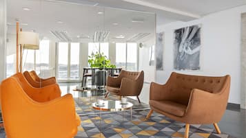 A modern office space with a large window, a round table, and two armchairs.