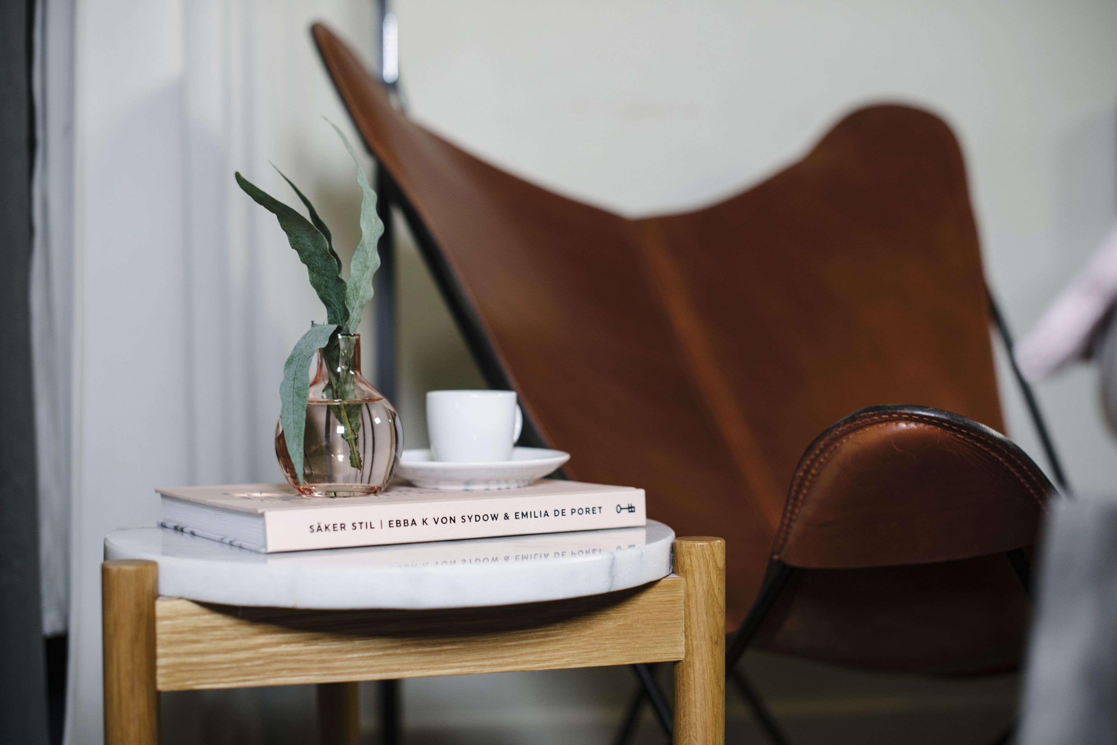 Una mesa con un florero, una taza, un platillo y libros.