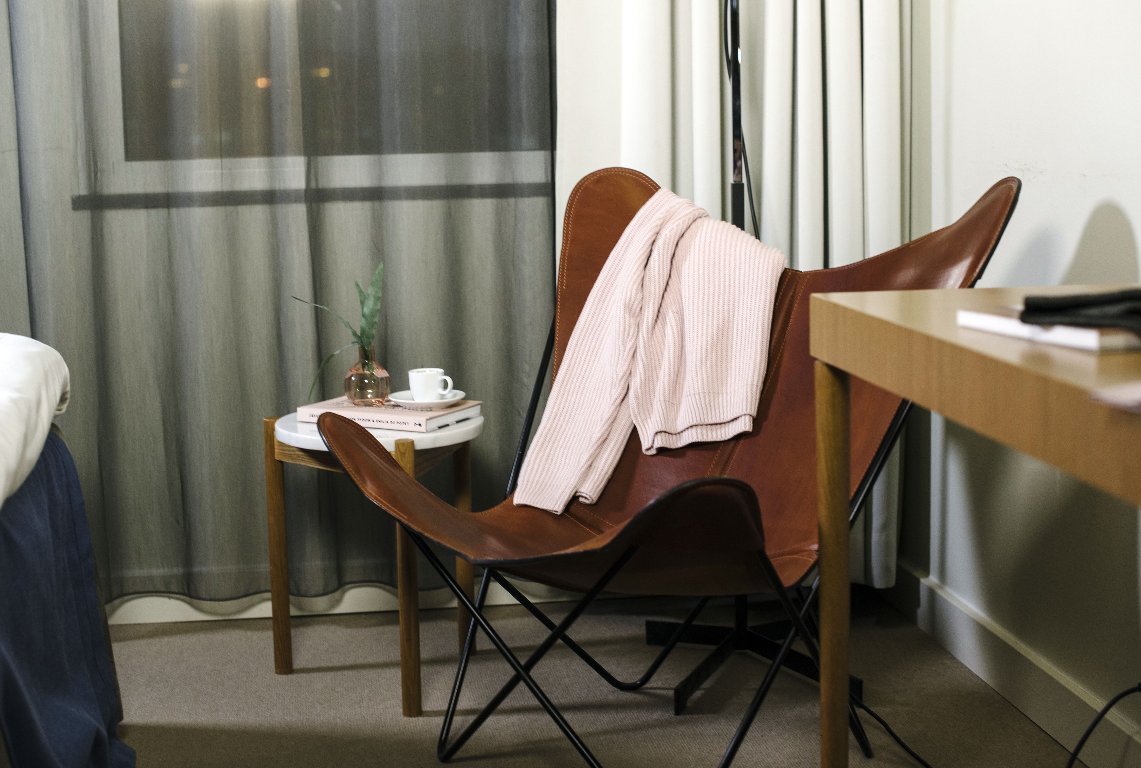 A modern room with a brown leather chair, a small round table with a plant, a white mug, and a book.