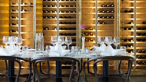 A restaurant with a long table set for dining, surrounded by chairs, and a wine cellar in the background. - Best Western Plus Sthlm Bromma (Bromma)