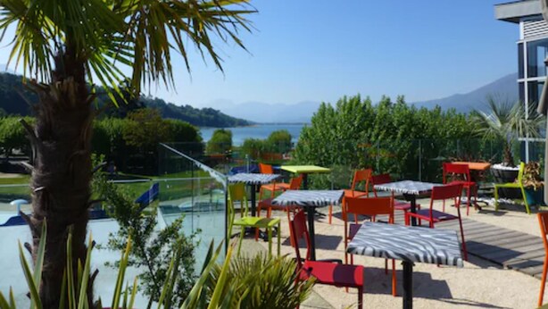Un espace extérieur aménagé avec des tables et des chaises, offrant une vue sur un plan d’eau et des montagnes.