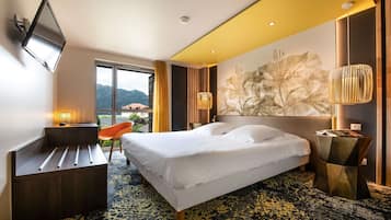 Habitación de hotel con cama, escritorio, silla y un gran ventanal con vistas a las montañas.