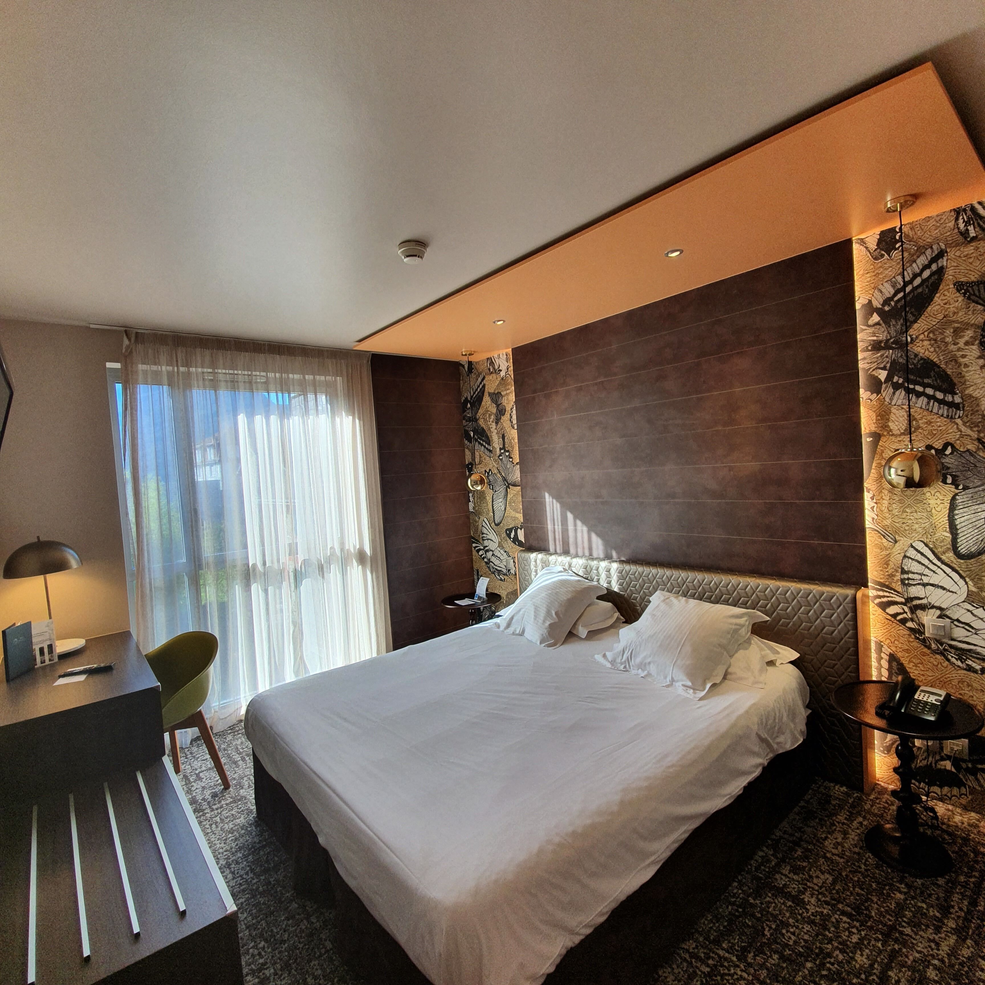 Een moderne hotelkamer met een groot bed, een bureau met stoel, een telefoon en een ventilator aan de muur.
