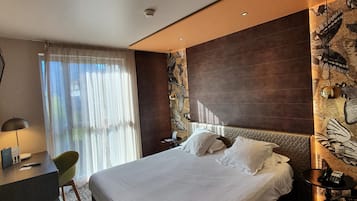 Een moderne hotelkamer met een groot bed, een bureau met stoel, een telefoon en een ventilator aan de muur.