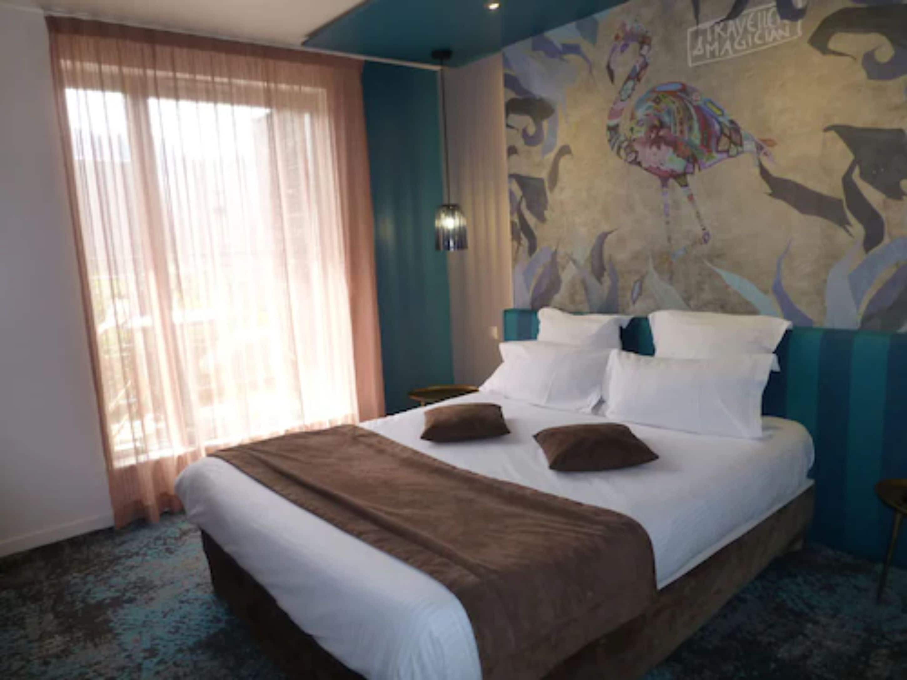 A hotel room with a large bed, a window with sheer curtains, a wall mural, and a patterned carpet.