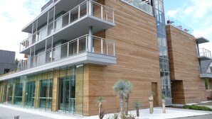 Un immeuble moderne à plusieurs étages, doté d’une façade en verre, de lambris en bois et d’un balcon avec des garde-corps en métal.