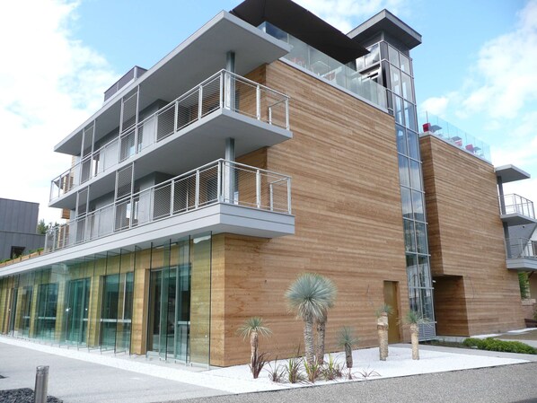 A modern multi-story building with a glass facade, wooden paneling, and a balcony with metal railings.
