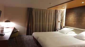 Una habitación de hotel con una cama, un escritorio con lámpara, una silla y una cortina.