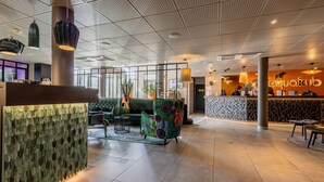 Un hall d’entrée moderne avec un comptoir d’accueil, un espace détente agrémenté de plantes et un mur décoré de motifs.