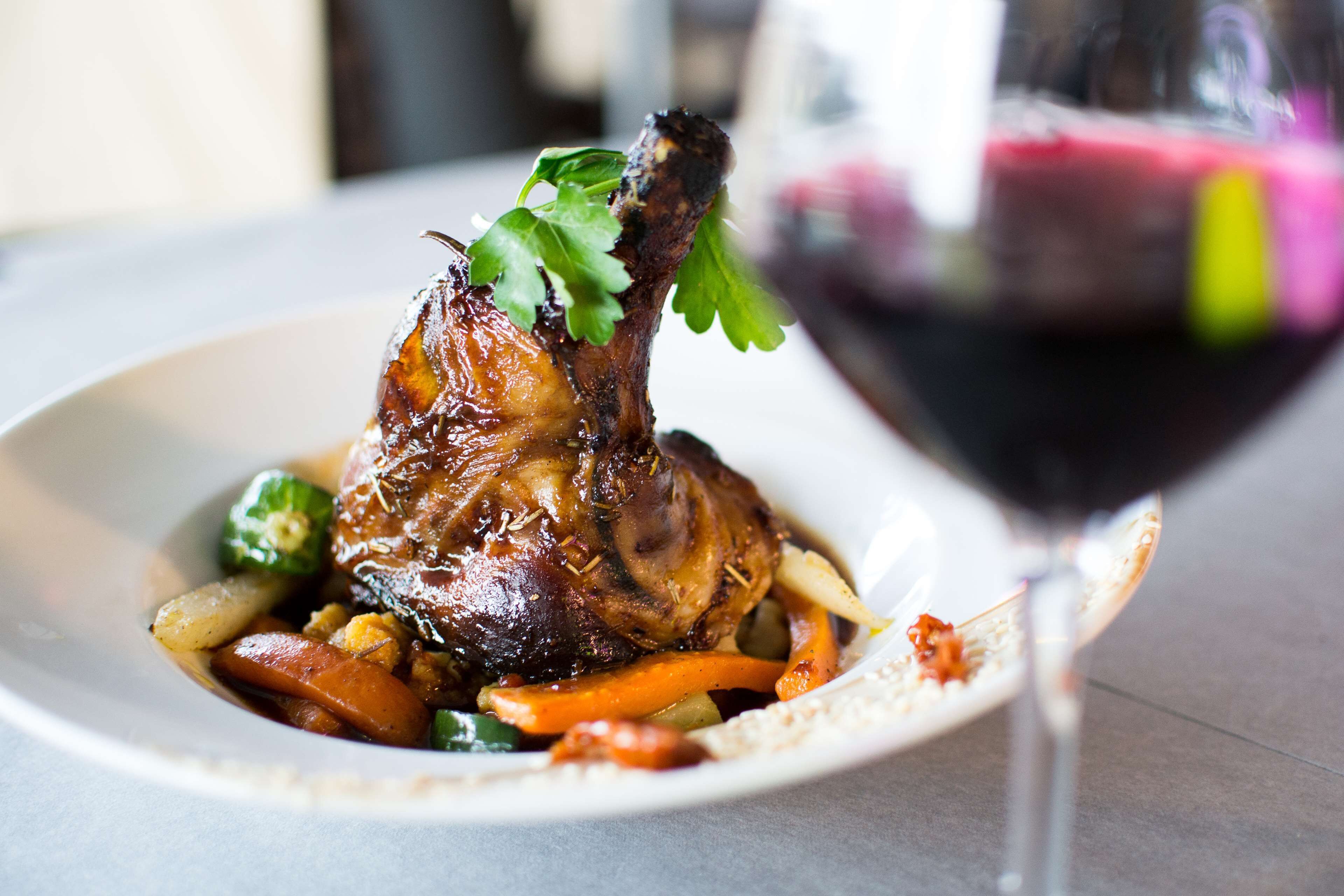 Une assiette de nourriture comprenant un gigot d’agneau rôti, des légumes et un verre de vin rouge.