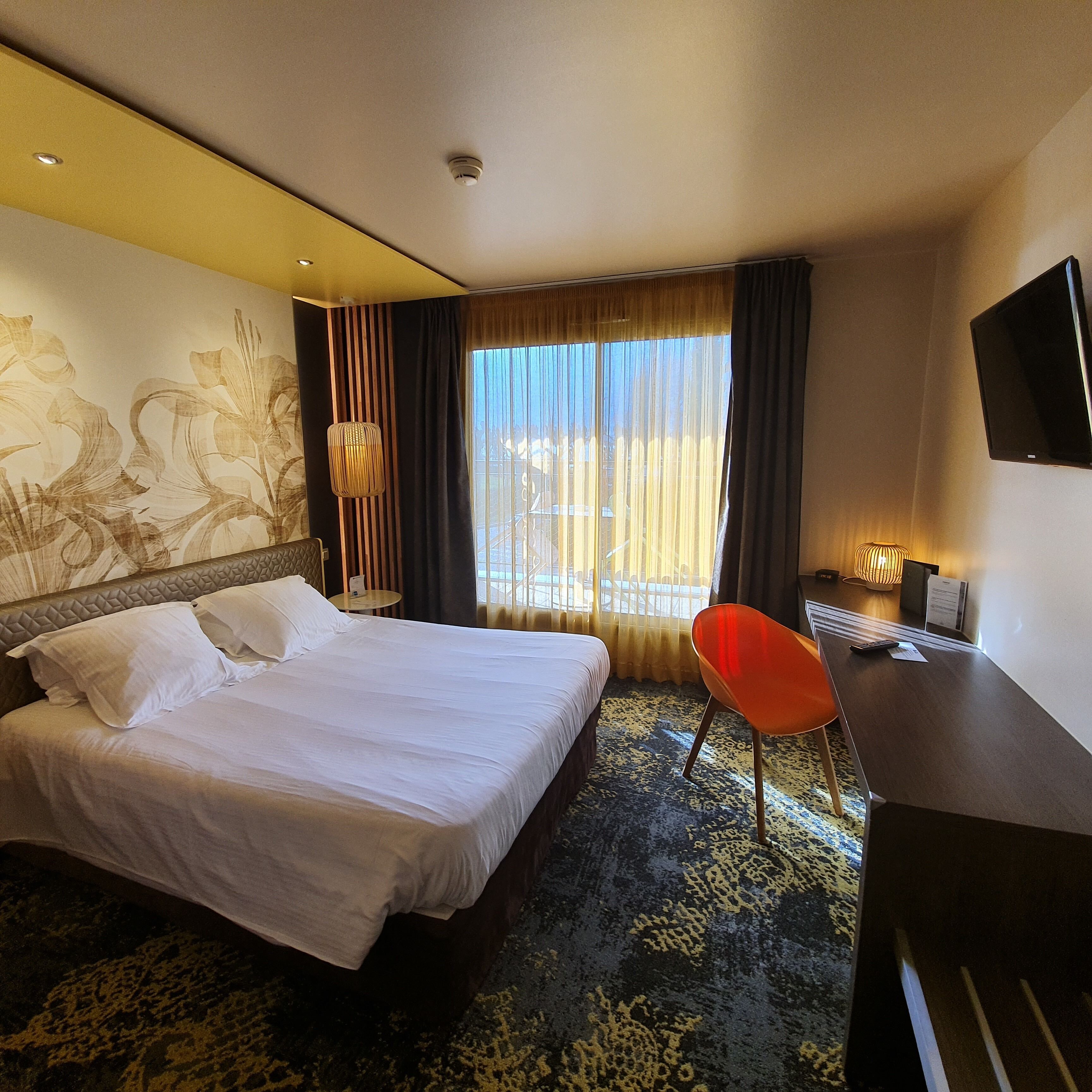 Habitación de hotel con una cama grande, un escritorio, una silla, un televisor y una ventana con cortinas.