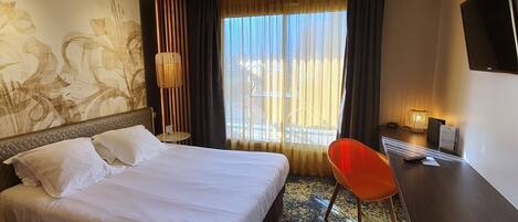 Habitación de hotel con una cama grande, un escritorio, una silla, un televisor y una ventana con cortinas.