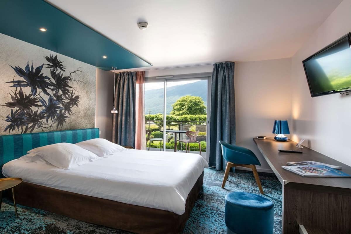 Une chambre d’hôtel équipée d’un lit, d’un bureau, d’une chaise, d’une télévision et offrant une vue sur l’extérieur.