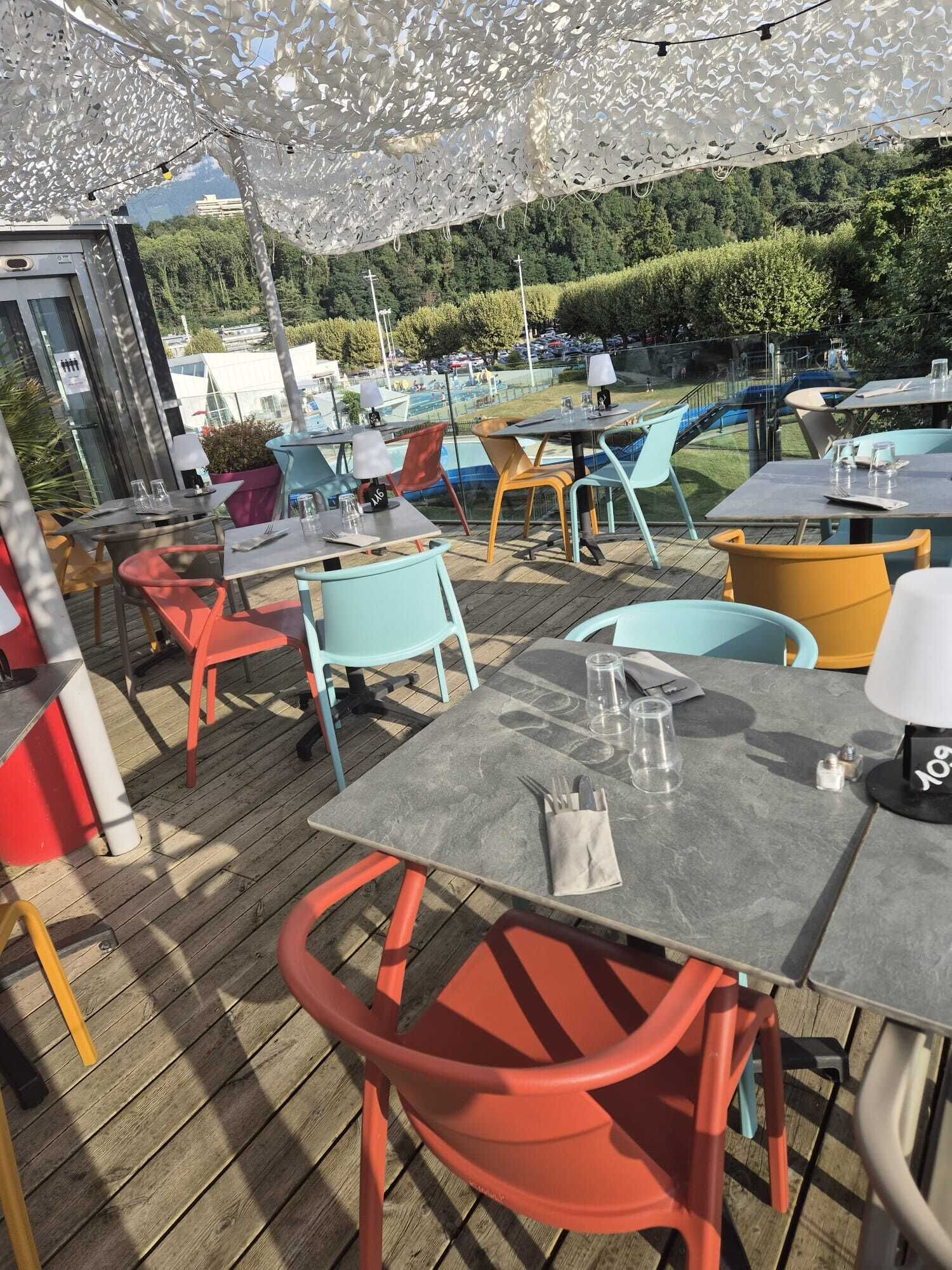 An outdoor dining area with tables and chairs, a pool in the background, and a view of the surrounding landscape.