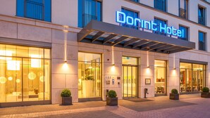 Een moderne hotelentree met een opvallend bord, grote glazen deuren en plantenbakken.