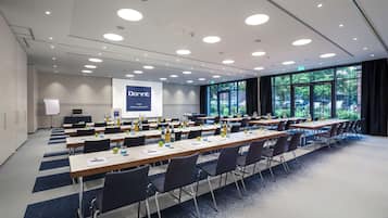 Ein Konferenzraum mit langen Tischen, Stühlen und einer Projektionsleinwand, auf der 'Dorint Hotel Hamburg-Eppendorf' angezeigt wird.
