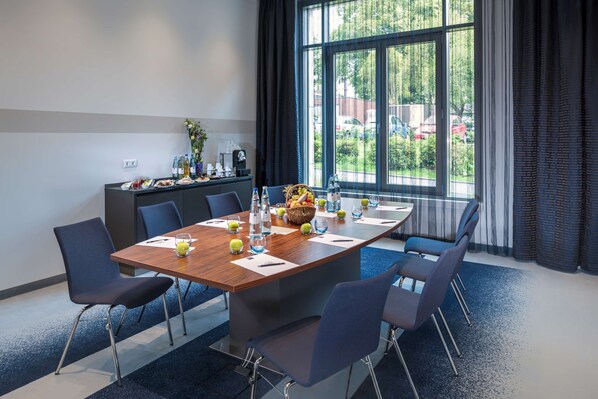 A conference room with a large table, chairs, and a view of the outdoors through large windows.