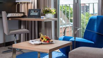 A hotel room with a desk, laptop, phone, and a fruit basket.