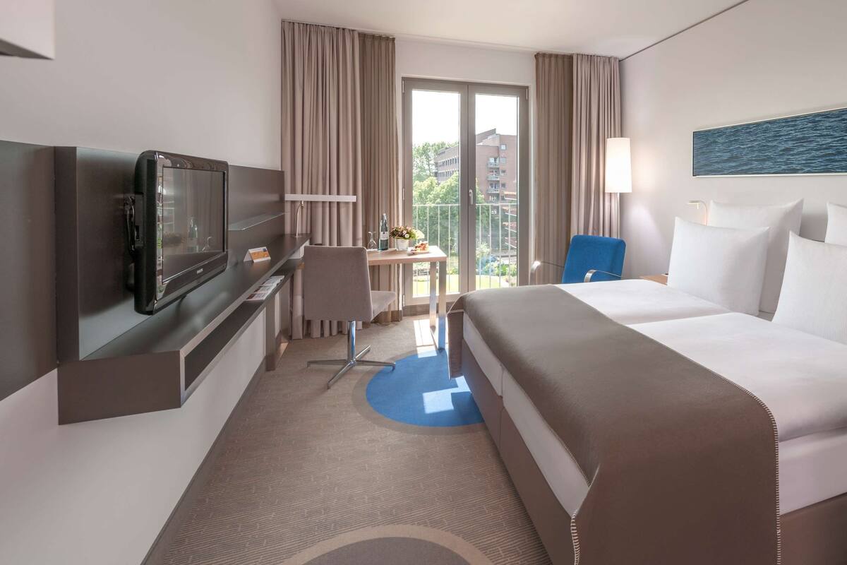 Une chambre d’hôtel avec un lit, un bureau et une chaise, une télévision et une vue sur l’extérieur.