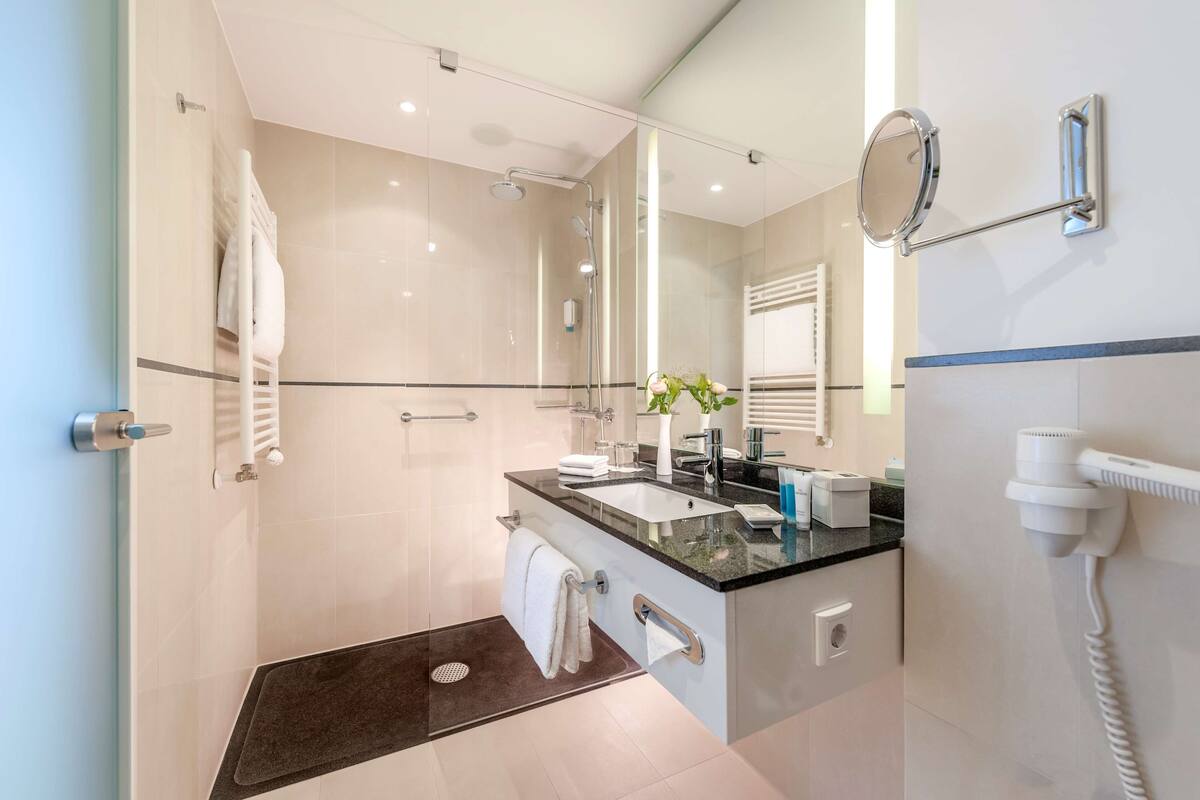 Une salle de bain moderne dotée d’une douche à parois de verre, d’un meuble-lavabo avec un évier, d’un miroir et d’un sèche-cheveux fixé au mur.