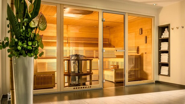 Een modern interieur met een schuifdeur naar een sauna, een houten bank en een plank met handdoeken.