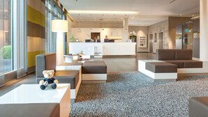 Een moderne hotellobby met zithoeken, een receptiebalie en een keuken op de achtergrond.