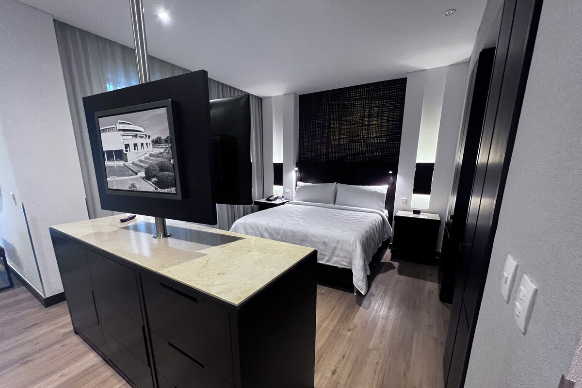 A modern hotel room with a bed, a TV, a desk, and a wardrobe.