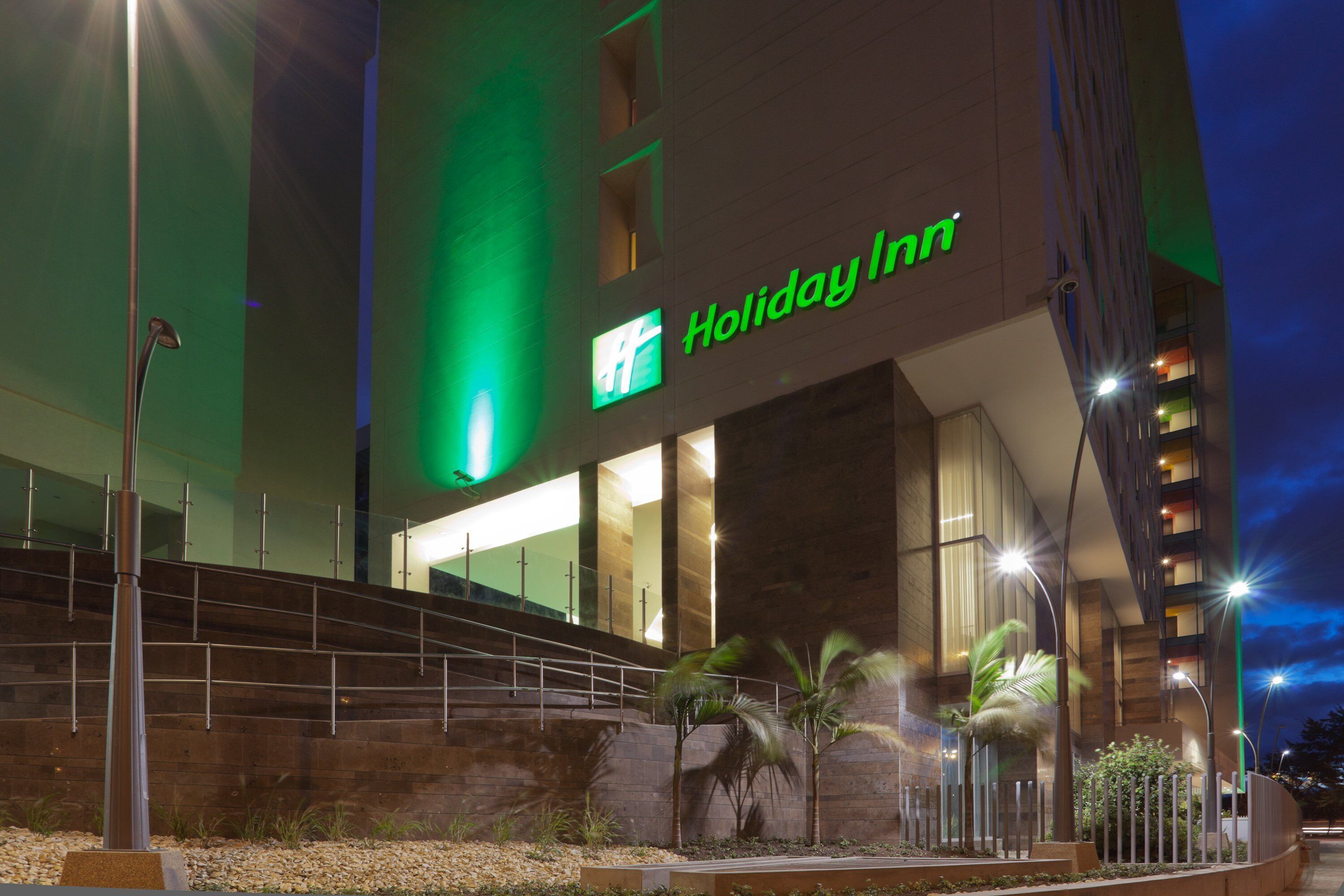 Un hôtel Holiday Inn doté d’une façade moderne, de grandes fenêtres et d’un escalier menant à l’entrée.