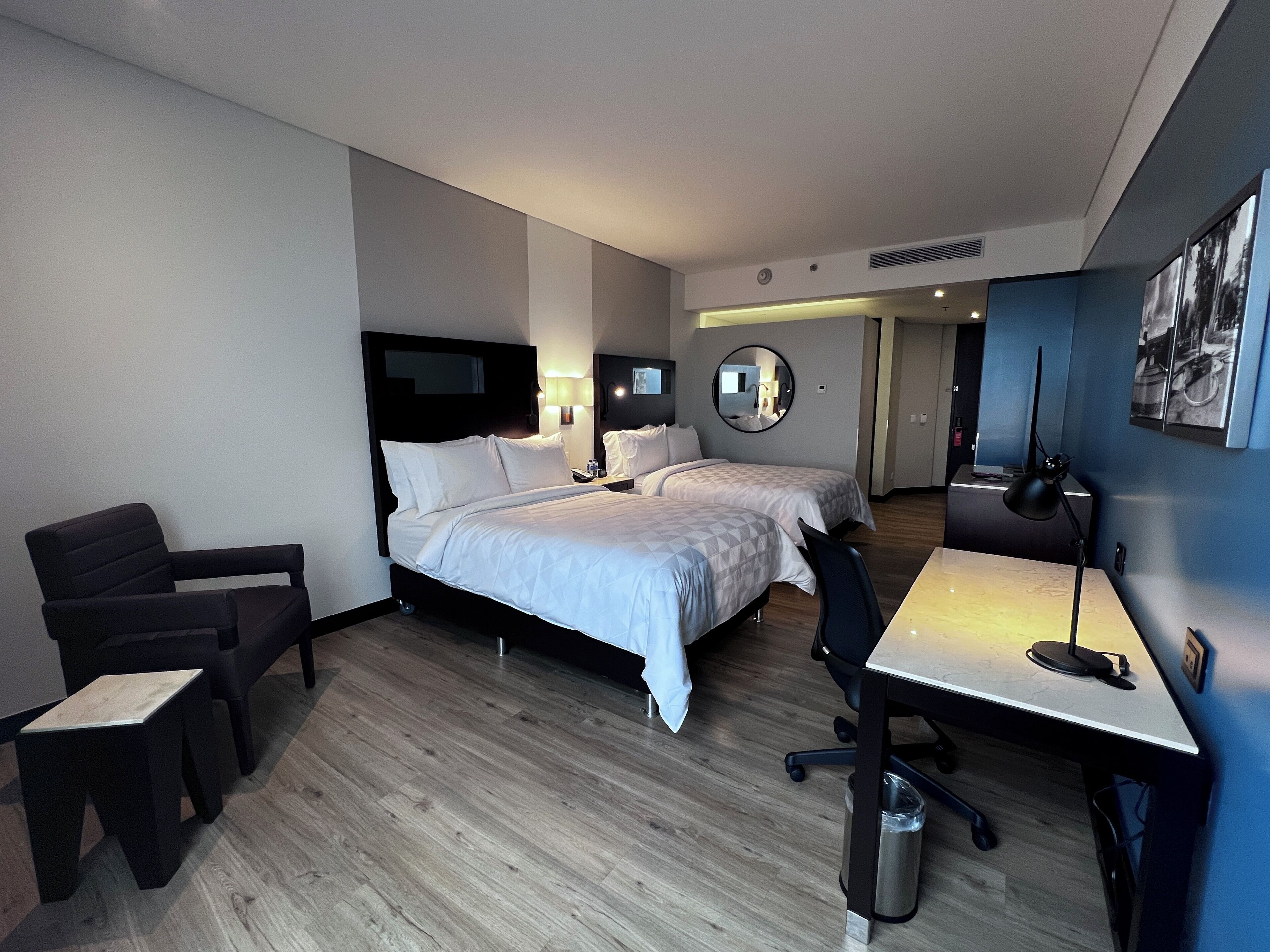 Habitación de hotel con dos camas, un escritorio, una silla, un televisor y un espejo.