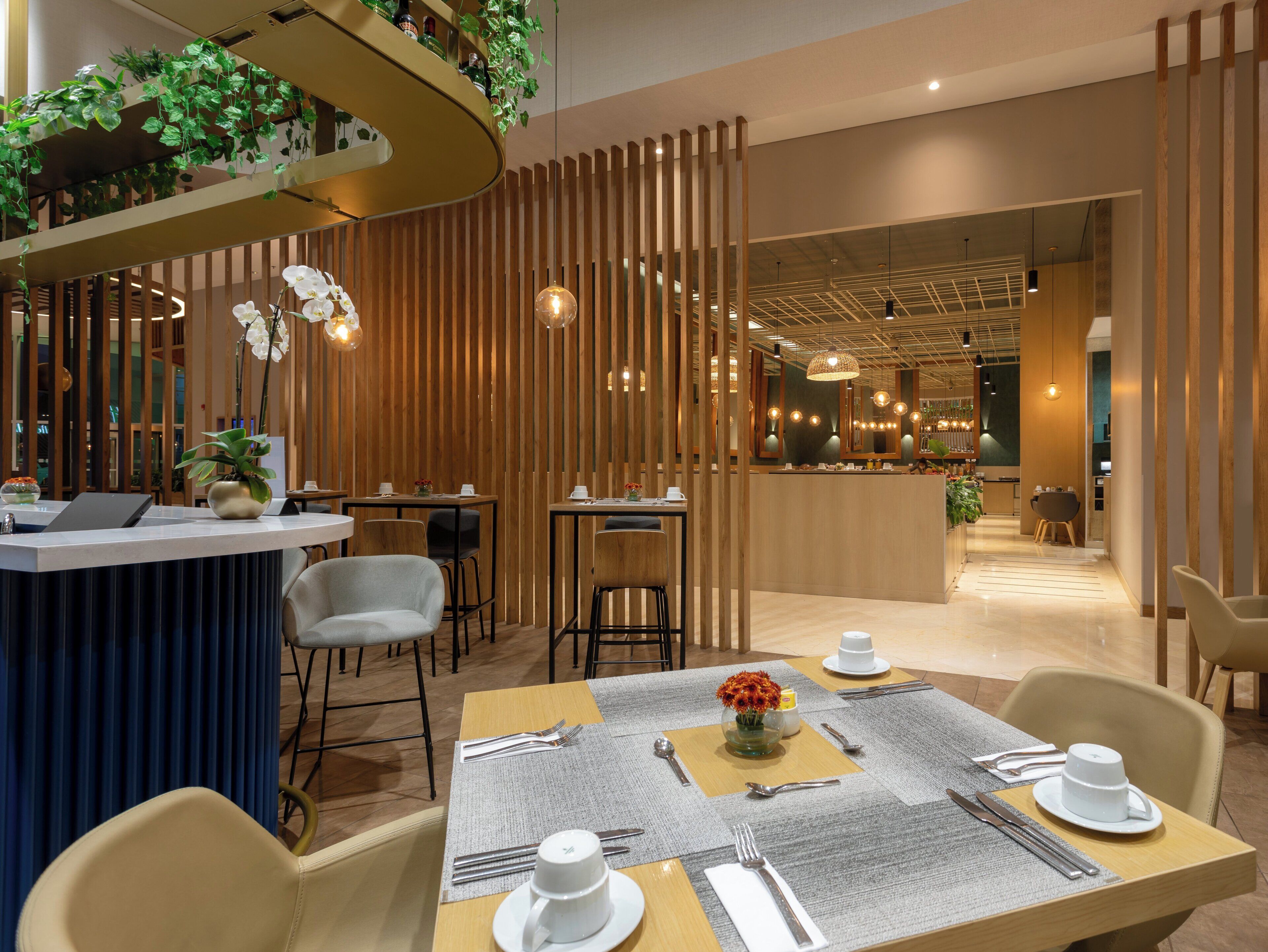 A modern restaurant interior with wooden paneling, a central bar area, and a seating arrangement with tables set for dining.