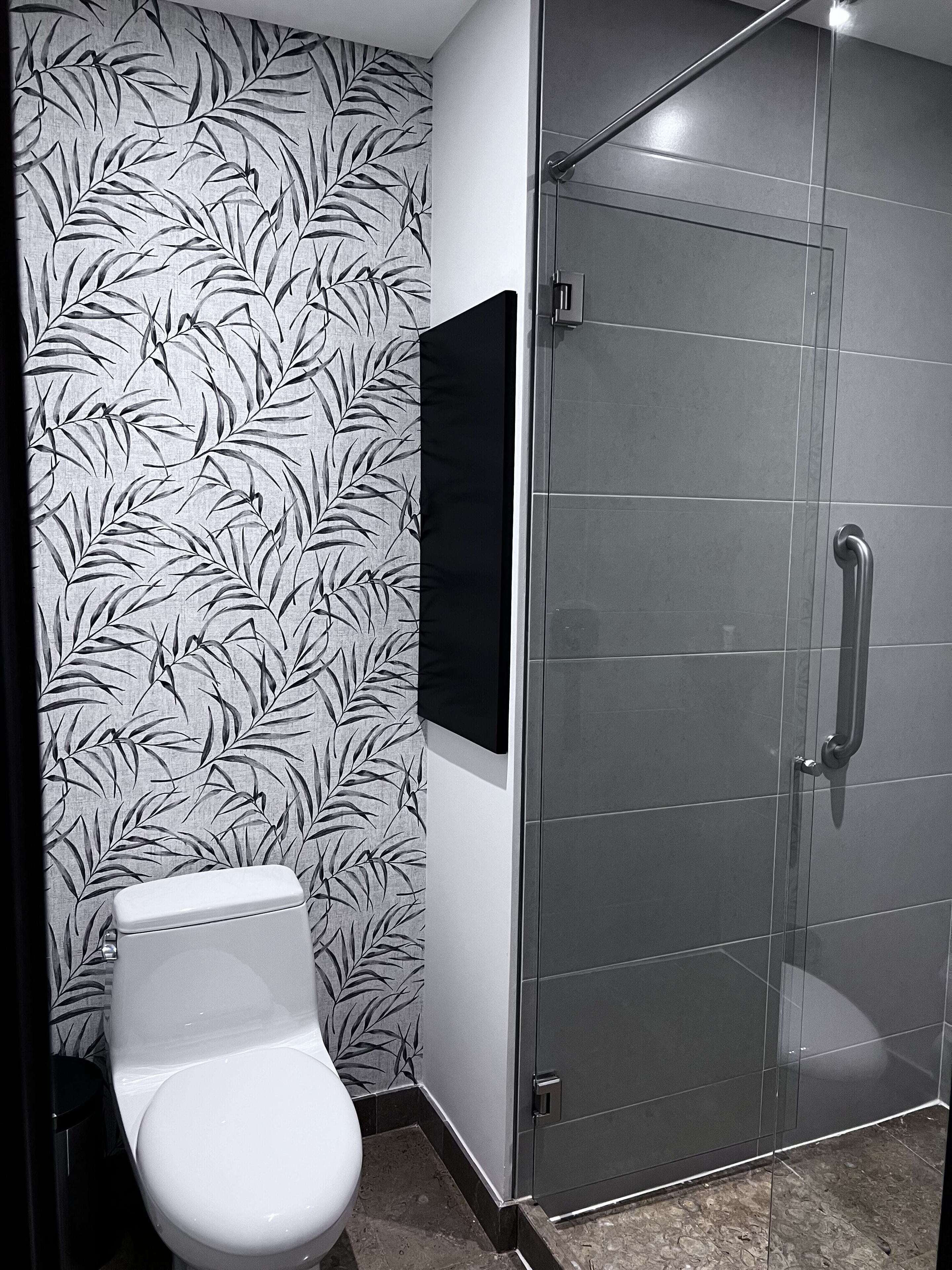 Een badkamer met toilet, een douchecabine van glas en een wand met bladmotief.